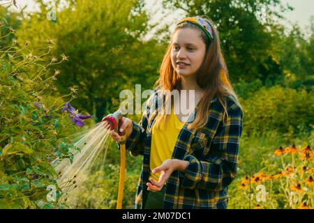 jeune jolie fille s'amusant dans le jardin arroser des plantes avec un tuyau. Souriant tout en prenant un passe-temps préféré Banque D'Images