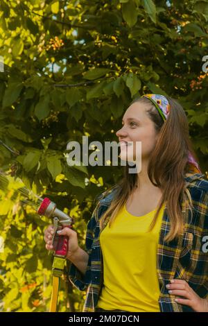 jeune jolie fille s'amusant dans le jardin arroser des plantes avec un tuyau. Souriant tout en prenant un passe-temps préféré Banque D'Images