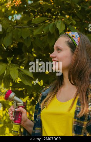 jeune jolie fille s'amusant dans le jardin arroser des plantes avec un tuyau. Souriant tout en prenant un passe-temps préféré Banque D'Images