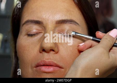 Maquilleuse applique une ombre à paupières . Belle femme visage. Main de visagiste, la peinture de cosmétiques de jeune fille modèle de beauté . Maquillage en cours Banque D'Images