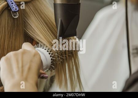 Gros plan du coiffeur mains séchage des cheveux humains avec l'équipement. Femme tenant un peigne. gros plan. Photo macro Banque D'Images