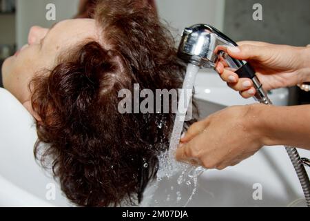 Magnifique gaie femme âgée bénéficie d'un massage de la tête tout en lavant ses cheveux par un coiffeur professionnel. Soins de beauté, coiffure, mode, style de vie Banque D'Images