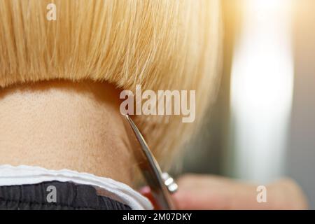 Gros plan d'un coiffeur coupe les cheveux blancs mouillés d'un client dans un salon. Coiffeur coupe une femme. Vue latérale d'un coupe de cheveux à la main avec des ciseaux Banque D'Images