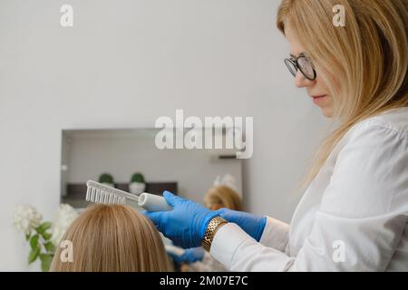 Le docteur examine la peau de tête d'une jeune fille avec un système spécial d'équipement de dermatologie, la perte de cheveux et trichologie concept femme analyse de cheveux avec Banque D'Images