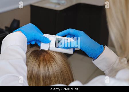 Vue rapprochée de la trichologue féminine examine la peau de la tête de la femme avec un système d'équipement spécial de dermatologie. Concept de perte de cheveux et de trichologie Banque D'Images