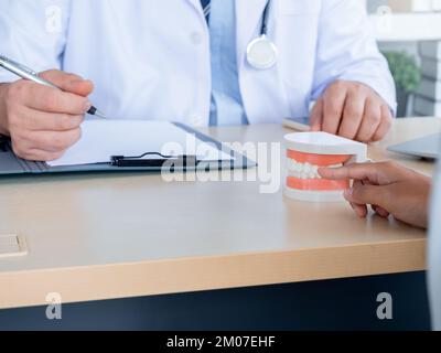 Gros plan sur un modèle de dent sur le bureau tandis que le dentiste écrit avec un document de dossier de patient sur la planchette à pince dans le bureau de clinique médicale avec un espace de copie. Coin-détente oral Banque D'Images