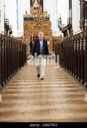 Dans la maison de Dieu. Portrait d'un homme âgé qui marche le long de l'allée d'une église. Banque D'Images