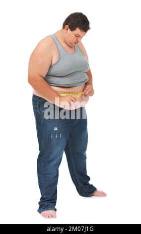 Regardant son poids. Un jeune homme obèse mesurant sa taille à l'aide d'un ruban de mesure sur fond blanc. Banque D'Images