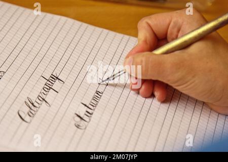 la main féminine écrit avec le stylo inky sur une feuille de papier blanche avec des rayures. papeterie sur le bureau vue rapprochée du dessus. leçons d'orthographe et calligraphie effort Banque D'Images