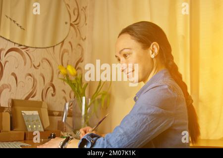 Une fille indienne écrit avec un stylo à encre. papeterie sur un bureau en bois. leçons d'orthographe et exercices de calligraphie. documents administratifs au bureau. l'étudiant écrit un let Banque D'Images