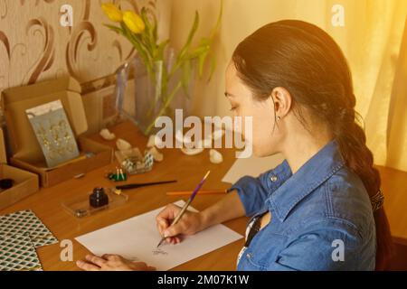 Une fille indienne écrit avec un stylo à encre sur une feuille de papier blanche. papeterie sur un bureau en bois. leçons d'orthographe et exercices de calligraphie. la paperasserie dans l'offic Banque D'Images