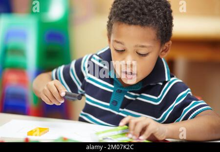 Son temps créatif. Avant l'école, un garçon afro-américain se concentrant sur ses dessins avec ses crayons et ses formes. Banque D'Images