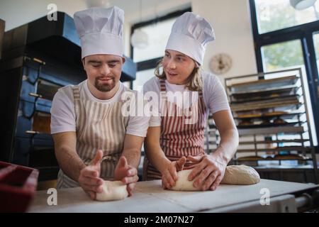 Homme avec le syndrom en bas aidant à précoupler le pain dans la boulangerie avec son collègue. Concept d'intégration les personnes handicapées dans la société. Banque D'Images