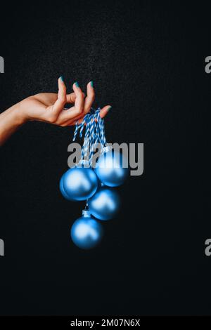 boules de noël dorées dans la main de la femme isolées sur fond noir. Couleur de l'année 2020 bleu classique. Concept tendance de couleur Pantone tendance Banque D'Images