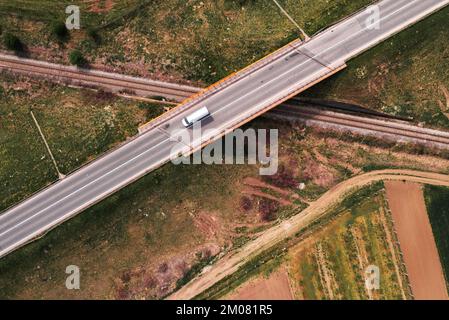 Minibus blanc traversant le passage supérieur du chemin de fer sur une autoroute vide, vue aérienne en haut à partir de l'image de drone pov pour le transport et le concept d'affaires de livraison Banque D'Images