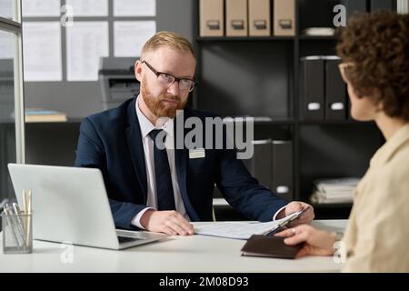 Portrait d'un consultant barbu à l'écoute d'une femme visitant l'agence Banque D'Images