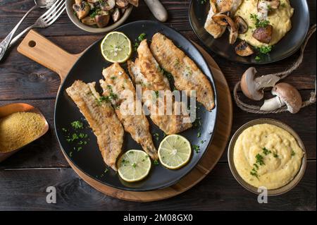 Poêler le poisson frit avec de la polenta et des champignons rôtis sur une table en bois. Pose à plat Banque D'Images