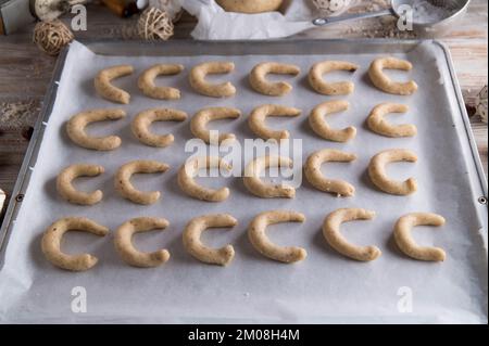 Biscuits de noël allemands, vanillekipferl ou croissants de vanille crus et non cuits sur une plaque de cuisson avec ustensiles de cuisine et décoration Banque D'Images