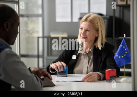 Portrait d'une femme mûre souriante consultante au bureau d'immigration de l'UE ou dans une agence gouvernementale et formulaires d'estampage Banque D'Images