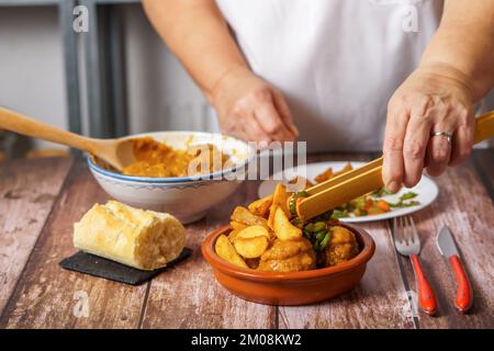 femme méconnaissable en tablier blanc servant des pommes de terre et des légumes sur une portion de boulettes de viande dans un plat en faïence Banque D'Images