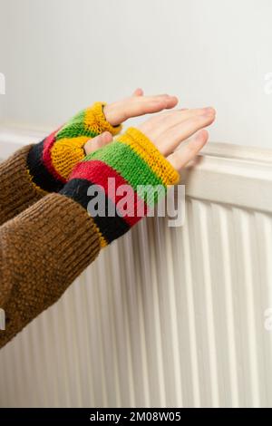 Gros plan des mains dans des gants sans doigts qui chauffent contre un radiateur à gaz Banque D'Images