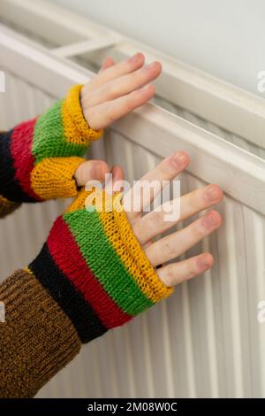 Gros plan des mains dans des gants sans doigts qui chauffent contre un radiateur à gaz Banque D'Images