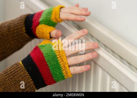 Gros plan des mains dans des gants sans doigts qui chauffent contre un radiateur à gaz Banque D'Images