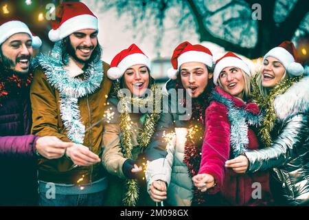 Groupe de jeunes qui applaudissent avec des spampers à l'heure de Noël - concept de style de vie d'hiver froid avec des amis heureux tendance portant des chapeaux de père noël rouges Banque D'Images