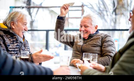 Des amis seniors jouent aux cartes au bar local le jour de l'hiver - concept de style de vie sans âge avec des personnes matures s'amusant ensemble - filtre de contraste lumineux Banque D'Images