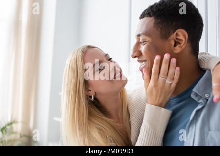 bonne femme blonde embrassant le petit ami afro-américain et touchant son visage dans la cuisine Banque D'Images