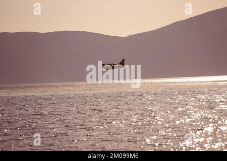 Un avion militaire survolant la mer avec des montagnes en arrière-plan pendant le coucher du soleil Banque D'Images