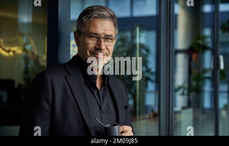 Portrait d'affaires - homme d'affaires en lunettes souriant au bureau, buvant du café. Âge mûr, âge moyen, homme adulte moyen en 50s avec un sourire heureux et confiant. Copier l'espace. Banque D'Images