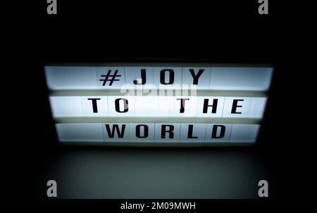 Boîte lumineuse avec l'expression « # Joy to the World » illuminée sur elle dans l'ombre et le fond sombre Banque D'Images