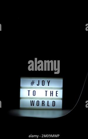 Boîte lumineuse avec l'expression « # Joy to the World » illuminée sur elle dans l'ombre et le fond sombre Banque D'Images