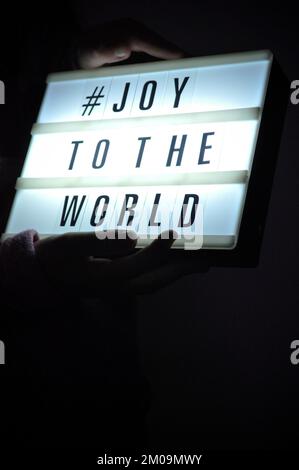 La boîte de lumière est tenue avec l'expression « # Joy to the World » illuminée sur elle dans l'ombre et le fond sombre Banque D'Images