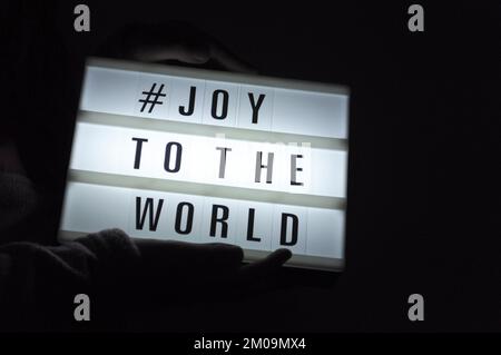 La boîte de lumière est tenue avec l'expression « # Joy to the World » illuminée sur elle dans l'ombre et le fond sombre Banque D'Images