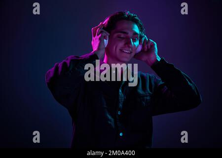 Portrait d'un jeune homme en chemise noire décontractée posé dans un casque isolé sur fond violet foncé dégradé dans une lumière néon. Concept de l'homme Banque D'Images