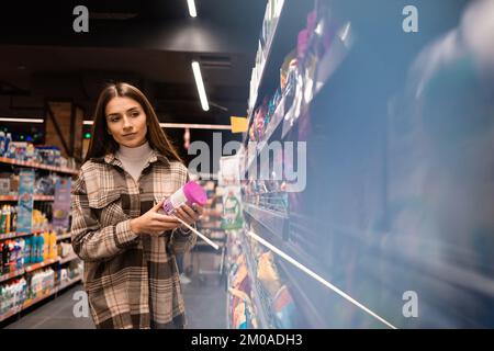 Une jeune femme choisit un produit de nettoyage dans un supermarché Banque D'Images