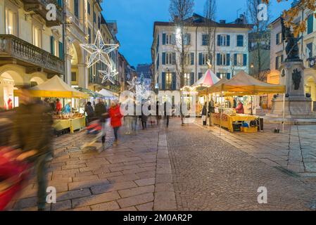 Shopping dans un marché de noël de rue avec des lumières de vacances au crépuscule. Ambiance de Noël dans le centre historique de Varèse, en Italie Banque D'Images