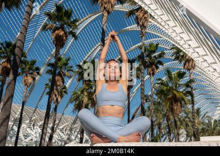 Femme méditant à la Cité des Arts et des Sciences, Valence, Espagne. Assis à pieds croisés au soleil Banque D'Images