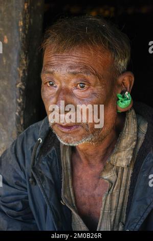 Mon district, Nagaland, Inde - 11 19 2010 : gros plan portrait de trois quarts de l'ancien homme de la tribu Naga Konyak avec grand perçage d'oreille tenant le sac de tabac Banque D'Images