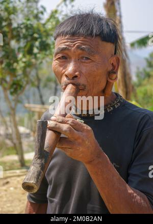 Quartier mon, Nagaland, Inde - 03 10 2014 : Portrait extérieur de l'homme de la tribu Naga Konyak avec un style de cheveux typique fumant traditionnel tuyau d'eau en bambou Banque D'Images