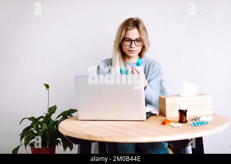 Portrait d'une jeune femme assise près d'un ordinateur portable, comprimés cloques, avoir un appel vidéo avec un médecin en ligne. Consultation en ligne. Banque D'Images