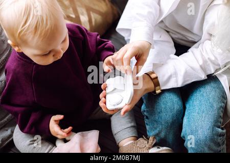 Vue de dessus de petite fille tout-petit assis sur un canapé, vue sur la boîte en plastique blanc. Médecin pédiatre montrant le thermomètre. Banque D'Images