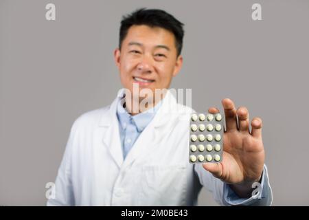 Un homme chinois souriant d'âge moyen, sous un manteau blanc, montrant des pilules, a recommandé un traitement médical Banque D'Images