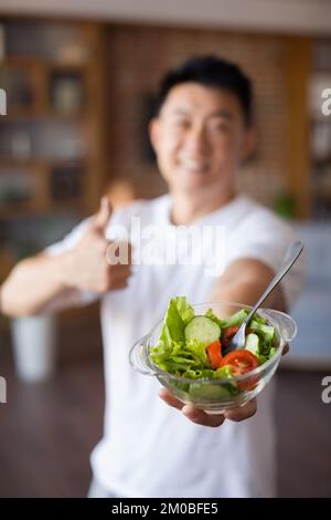 Alimentation saine de forme physique. Homme asiatique mûr et enthousiaste tenant un bol avec une salade de légumes frais et montrant le pouce vers le haut Banque D'Images