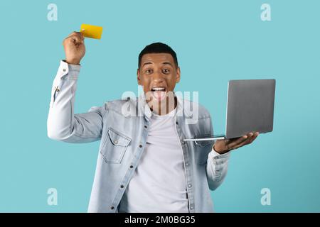 Joyeux jeune afro-américain excité dans une ambiance décontractée avec le bouche ouverte avec ordinateur portable, hurlant, célébrez la victoire Banque D'Images