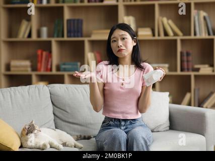 Contrarié femme coréenne tenant le papier de soie, ayant allergique à la fourrure et souffrant de nez de course causé par son chat d'animal de compagnie Banque D'Images