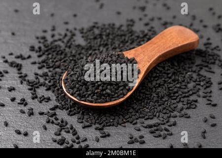 Graines de cumin noires dans une cuillère en bois sur fond noir. Nigella sativa pour Ayurveda et la médecine à base de plantes et. Graines de Kalonji pour la cuisine. Macro. Banque D'Images