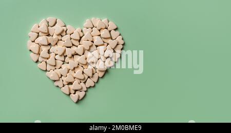 Compléments nutritionnels pour animaux en forme de cœur sur fond vert. Friandises vitaminées pour chats et chiens macro. Concept de pilules vétérinaires naturelles. Banque D'Images